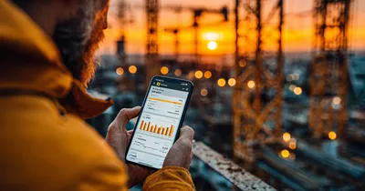 Site manager hands holding a smartphone showing a project dashboard on a construction site at golden hour